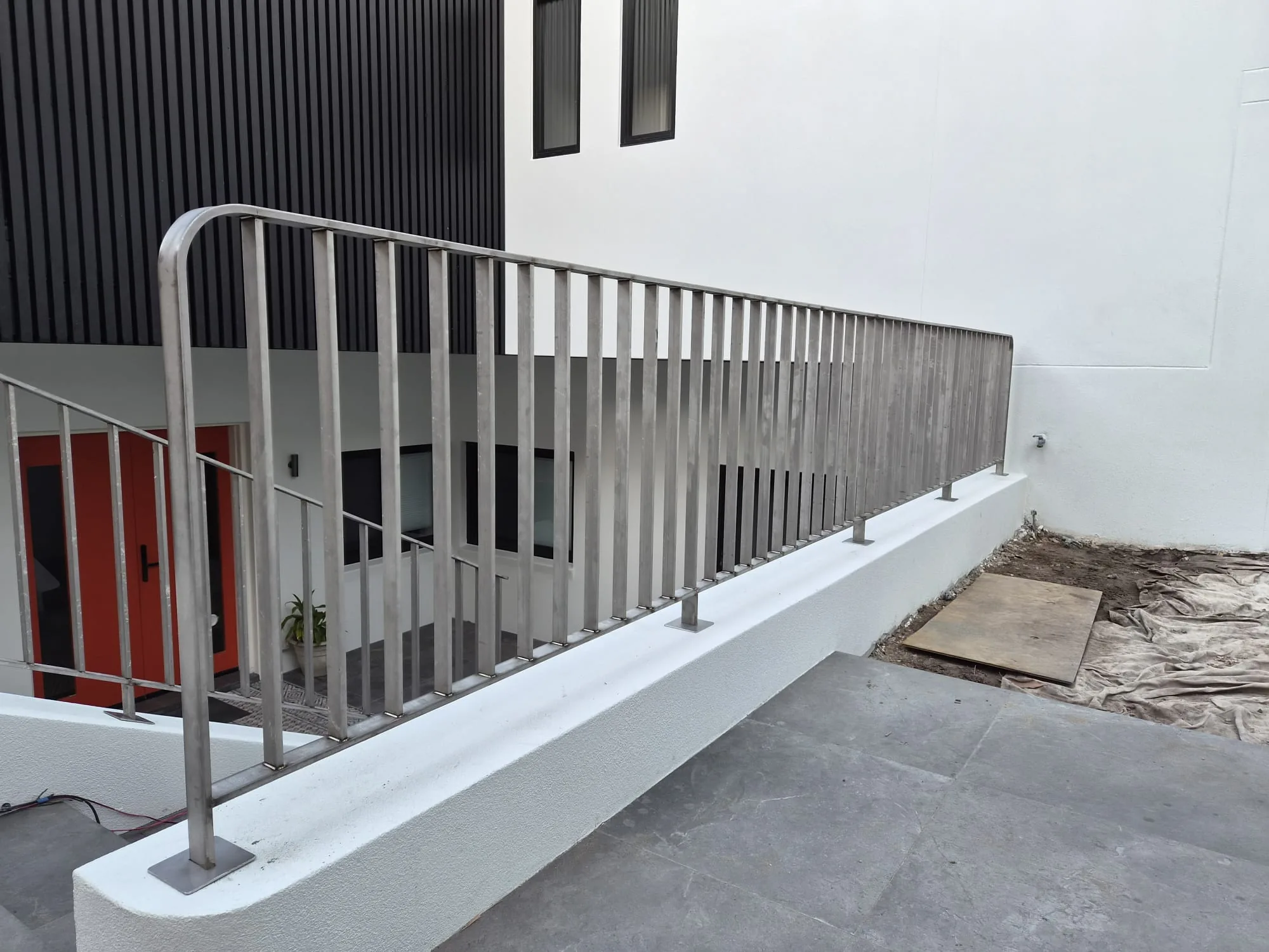 Exterior entry stairs with a stainless vertical-bar balustrade beside black cladding.