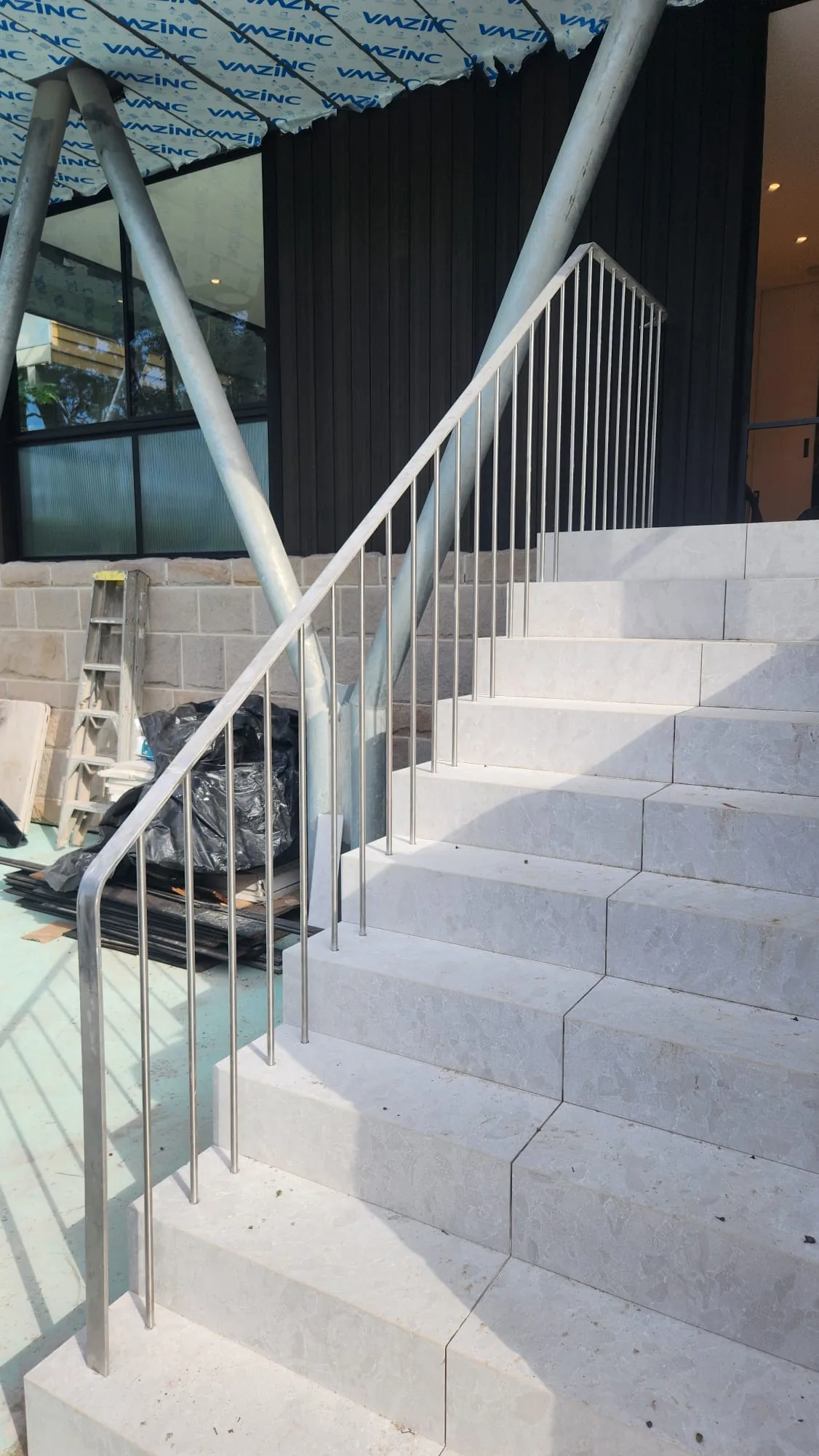 Interior stone stairs with a stainless rod balustrade against a black feature wall.