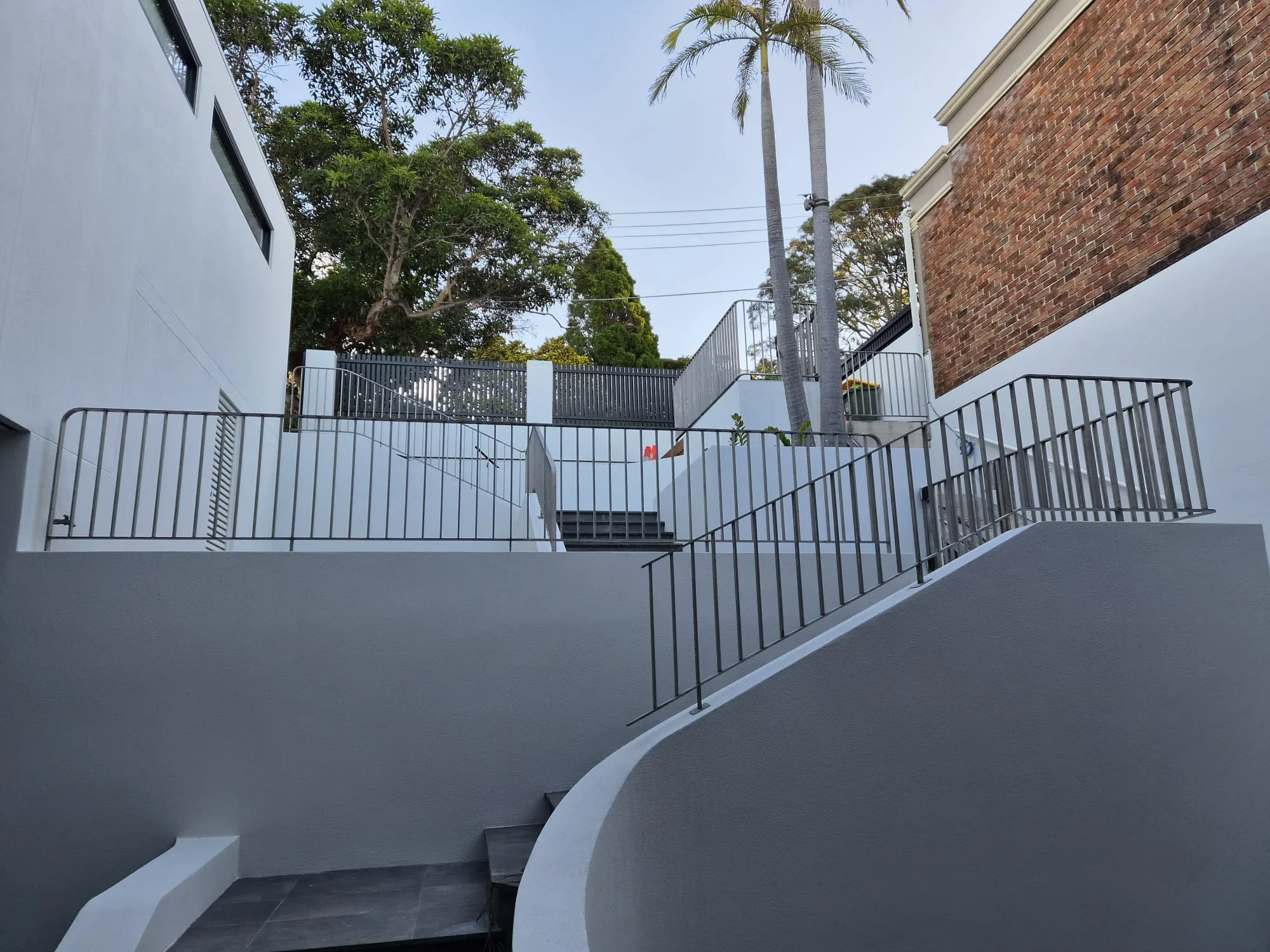 Metal handrail following a curved exterior ramp and rendered wall.