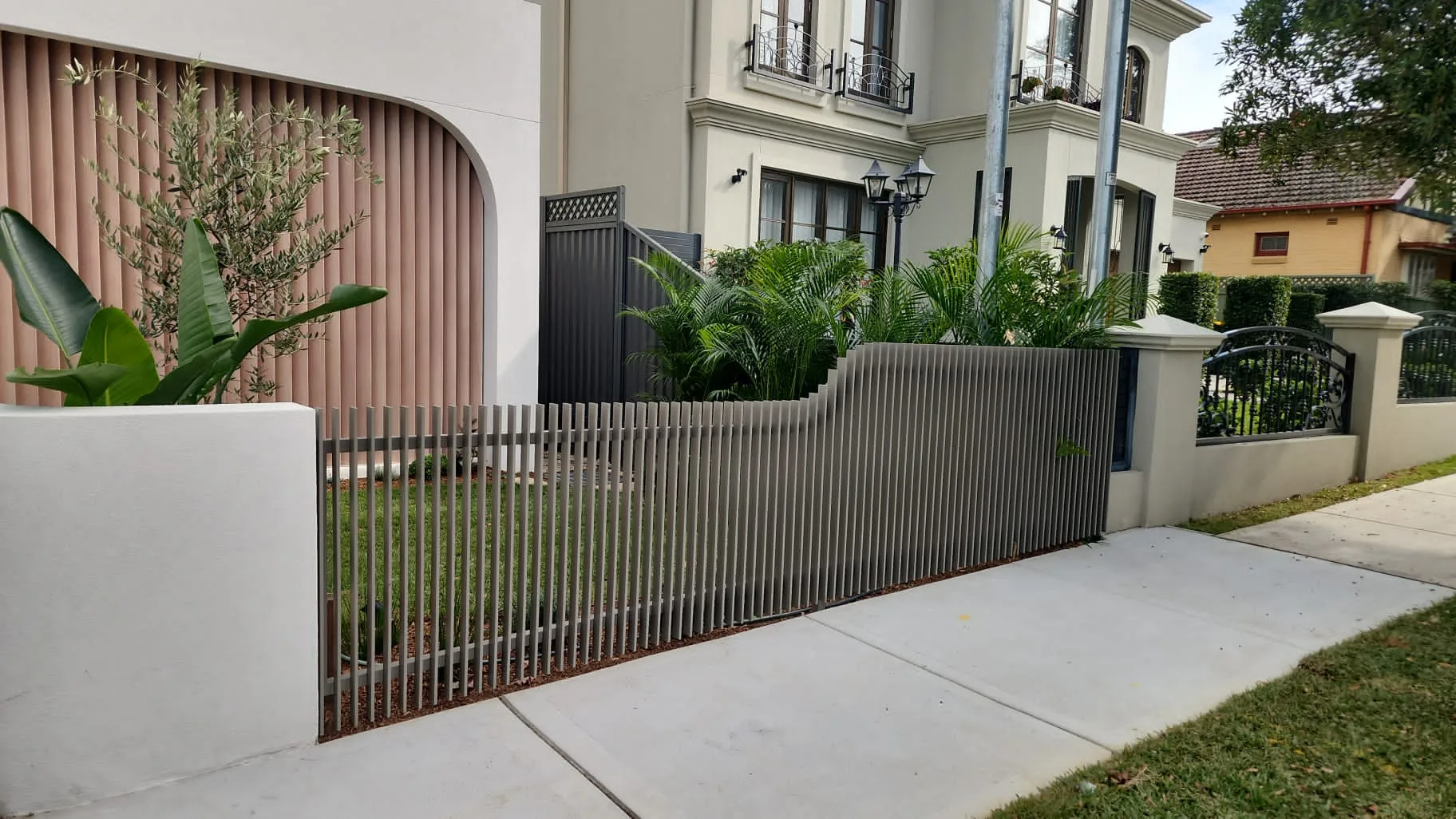 Aluminium slat fence atop a rendered wall to a garden frontage.