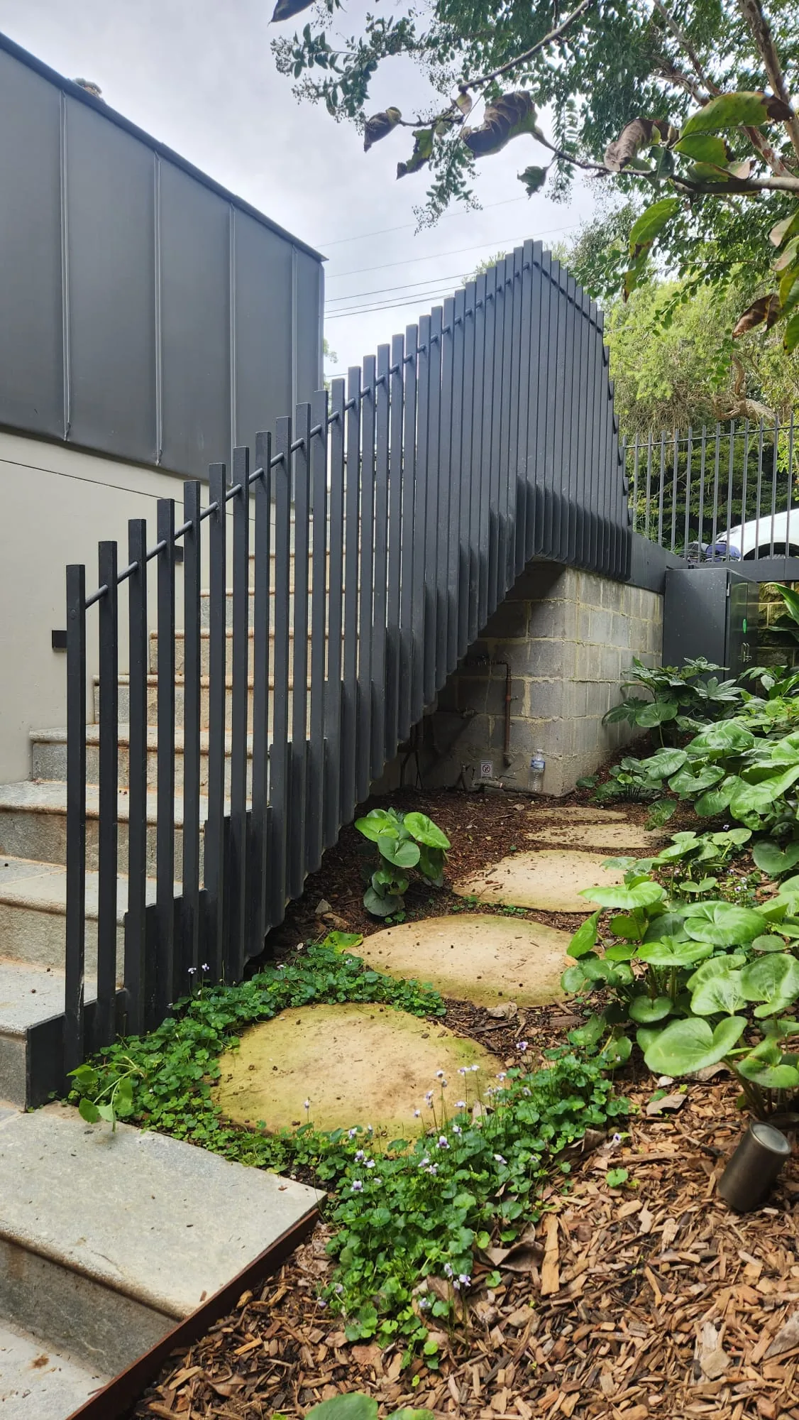 Black steel bar fence beside garden stepping stones.