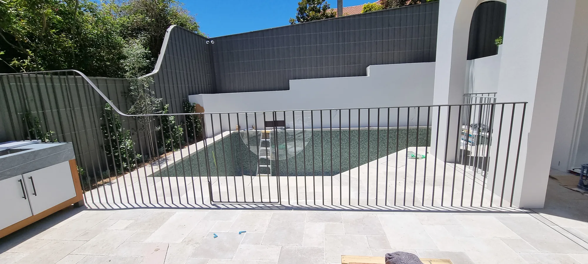 Black steel vertical-bar pool fence and balustrade around a courtyard pool.