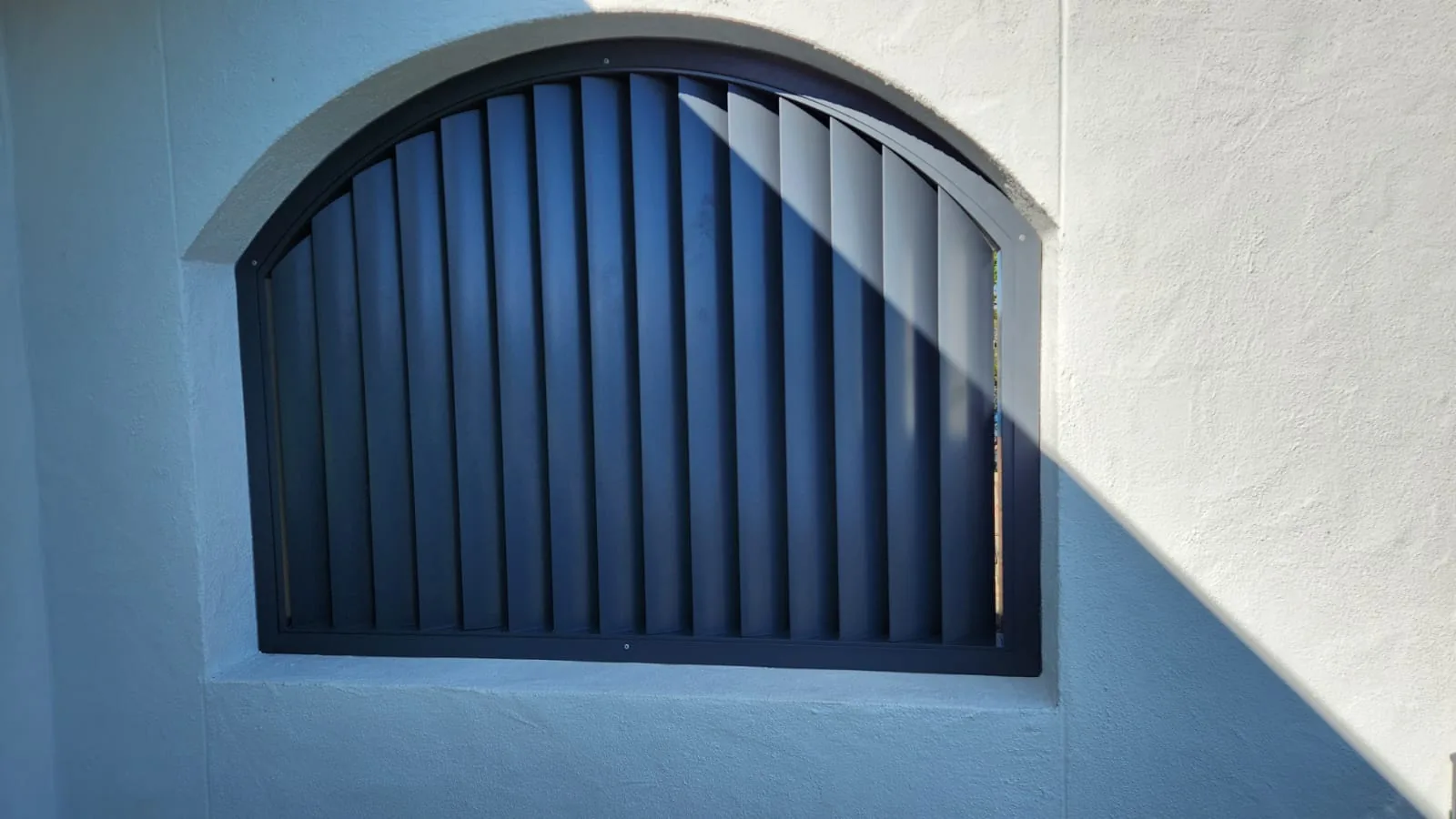 Arched semi-circular louvred steel screen on a white rendered wall.
