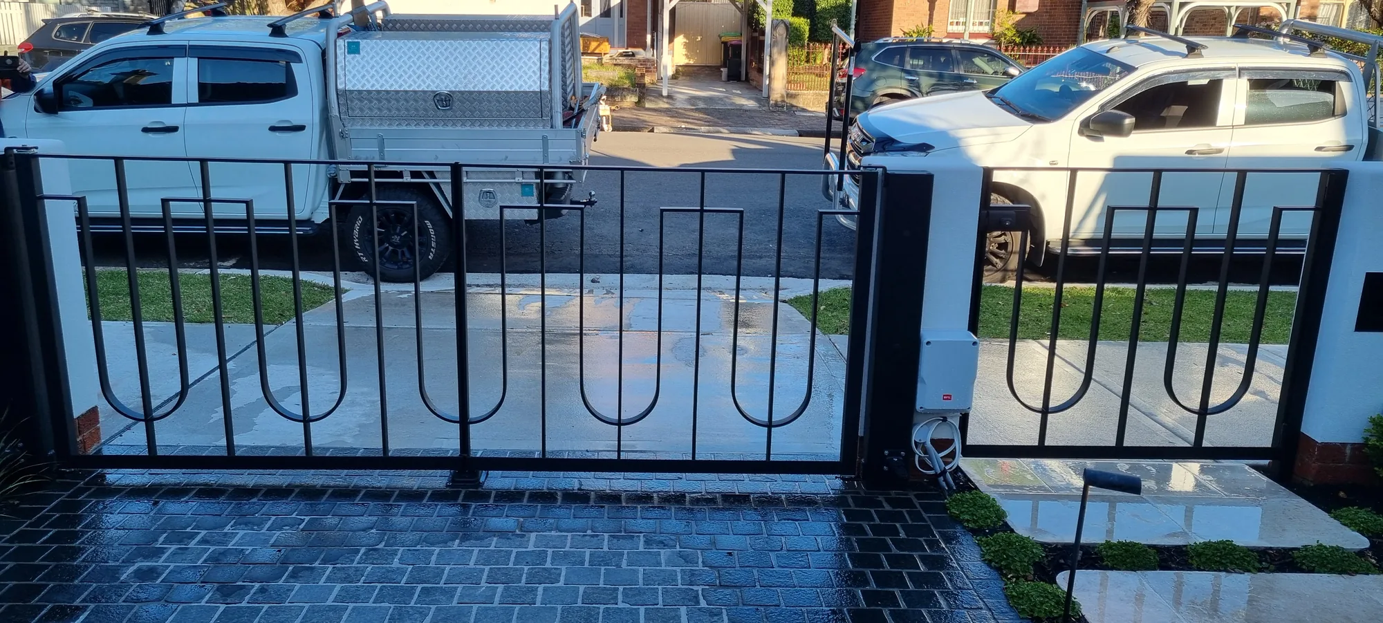 Black steel driveway and pedestrian gates with a decorative curved pattern, street frontage.