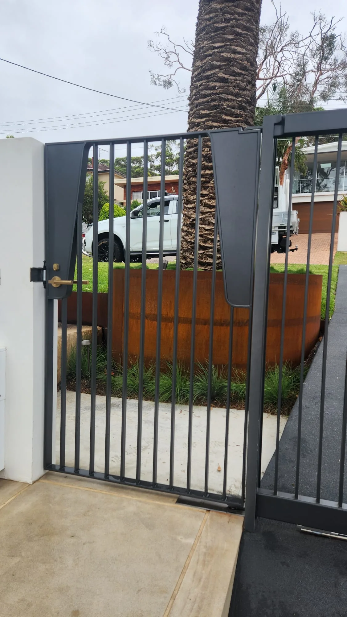 Black steel vertical-bar driveway gate at a property entrance.