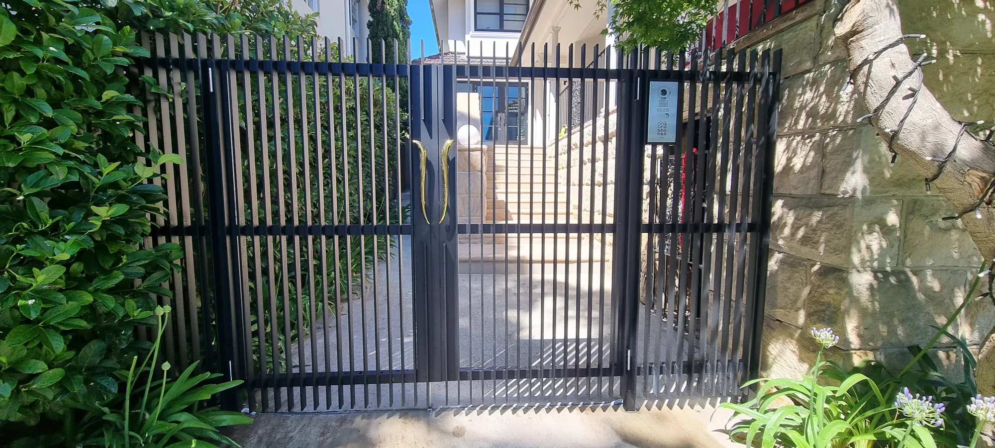 Black steel vertical-bar driveway gate set between hedges.