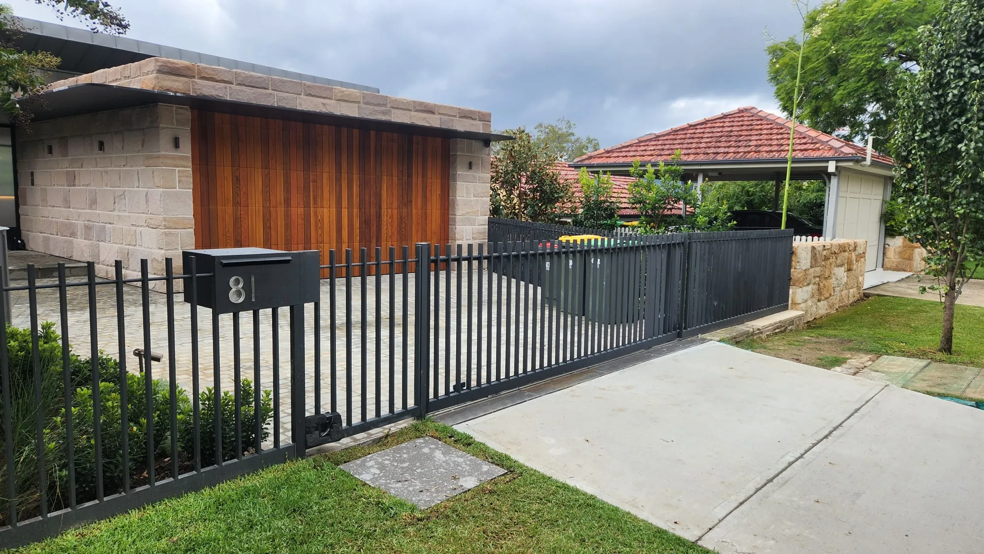 Black steel driveway gate and fence alongside timber cladding.