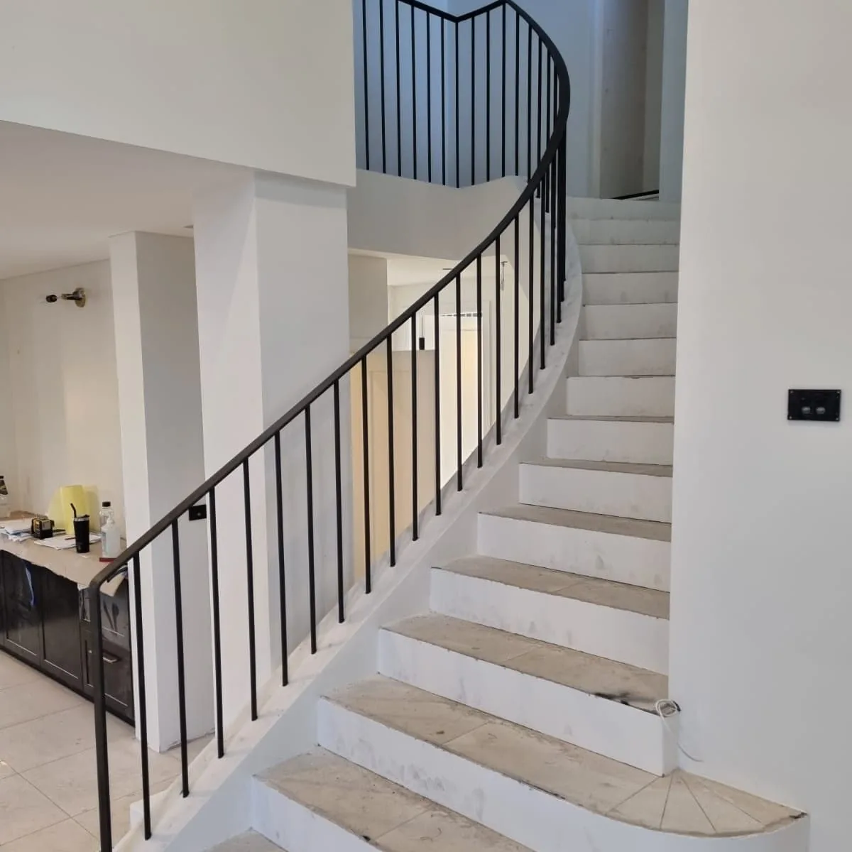 Elegant curved interior staircase with stone treads and a slim black steel balustrade.
