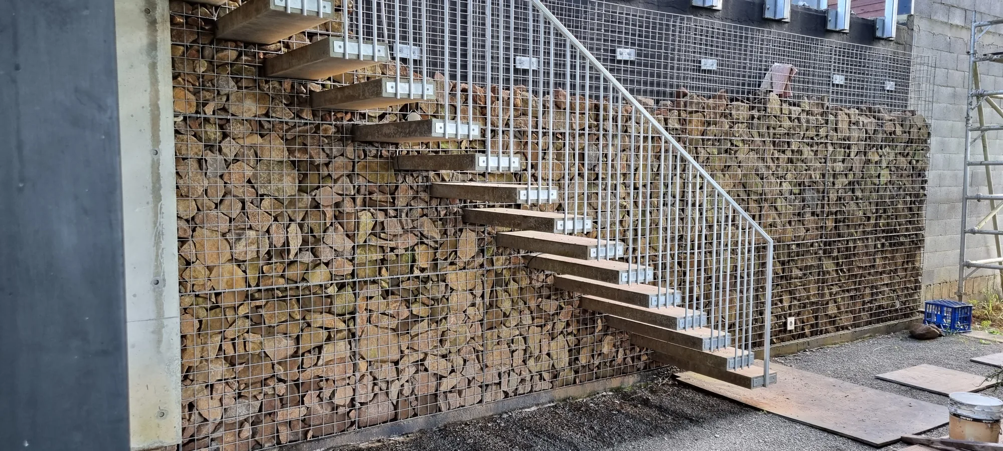 Cantilevered floating steel stair treads mounted to a stacked-stone feature wall with a tensioned wire balustrade.