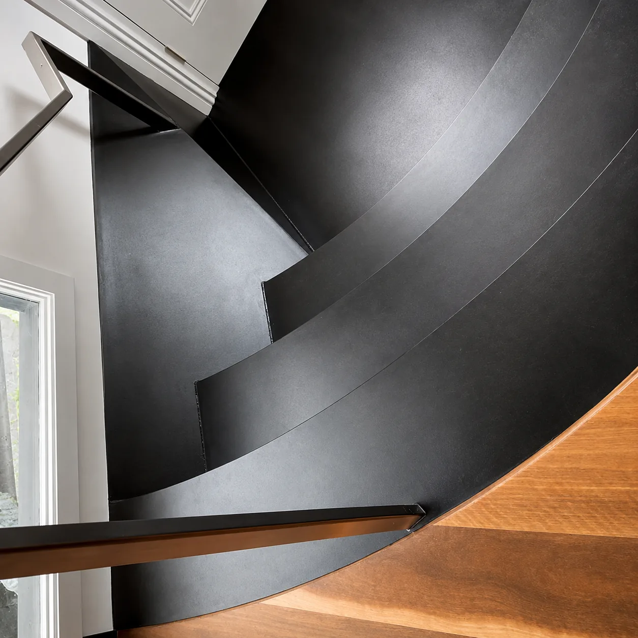 Curved blackened folded-steel staircase over a timber floor.