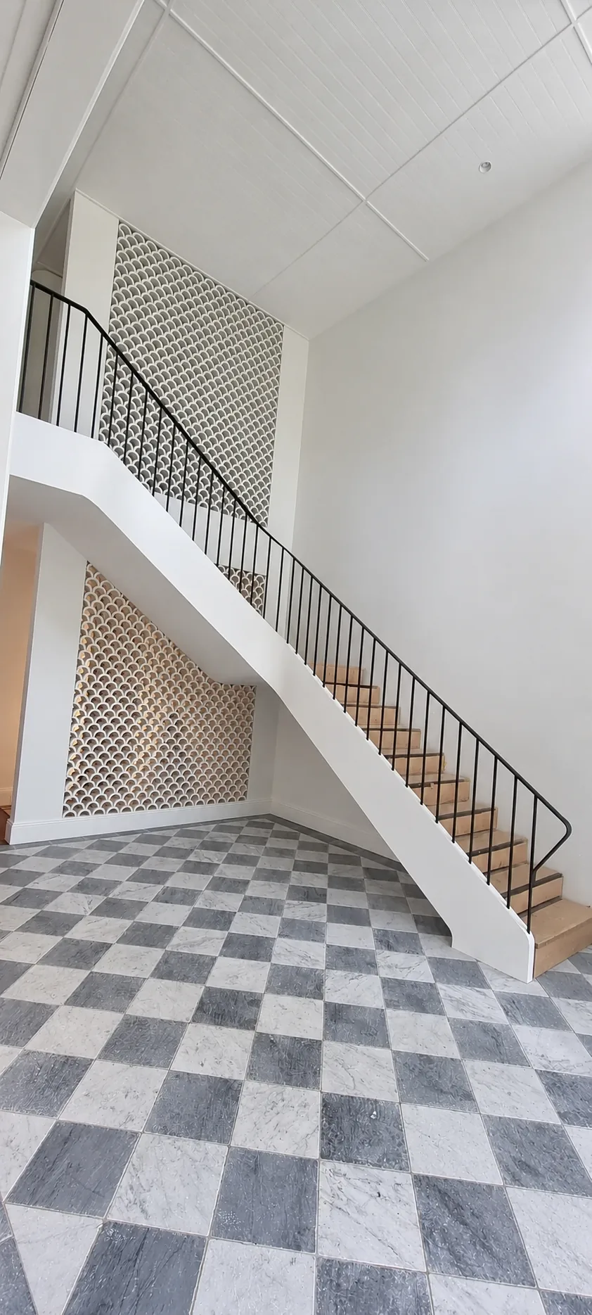 Modern interior steel staircase with perforated metal treads over a checkerboard floor.