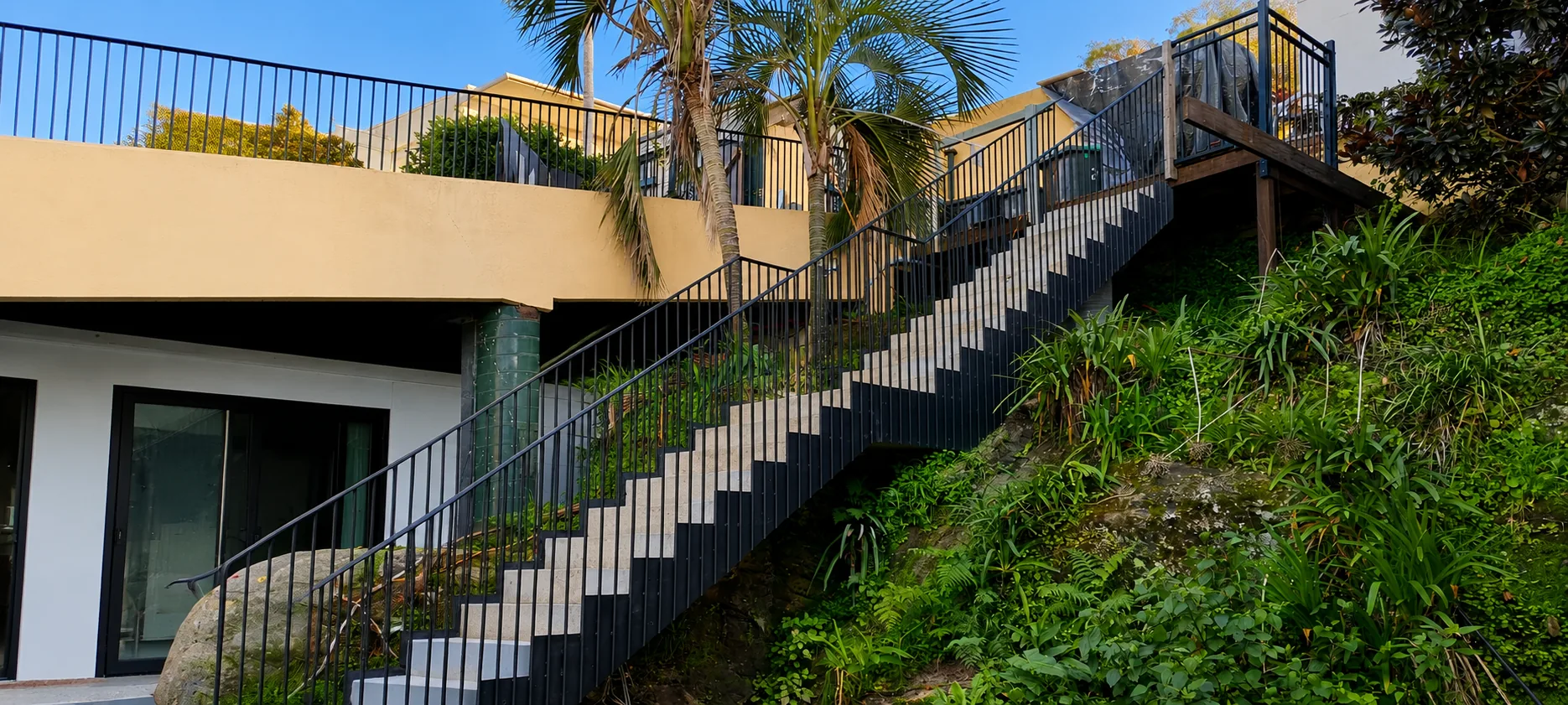 Exterior steel staircase running up a landscaped slope between buildings.