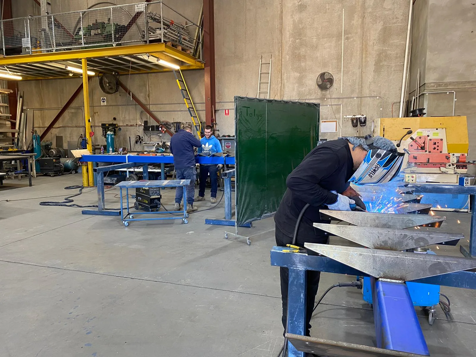 The Sydney Welding team fabricating steel stair components at the benches behind welding screens